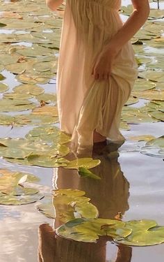 a woman is standing in the water with lily pads on her feet and wearing a white dress