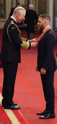 two men in suits and ties standing next to each other on a red carpeted floor