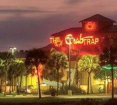 the crab trap is lit up at night in front of palm trees and other buildings