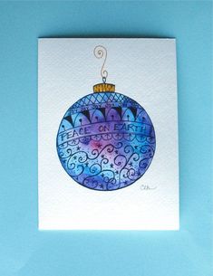 a blue christmas ornament hanging on a white card against a light blue background