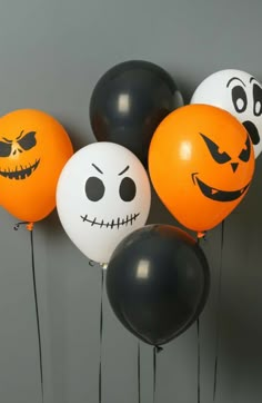 halloween balloons with faces on them are hanging from the ceiling in front of a gray wall