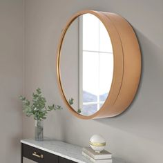 a round mirror hanging on the wall above a console table with a vase and flowers