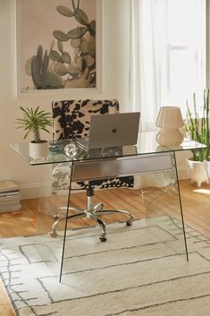 a glass desk with a laptop on it in front of a chair and potted plant