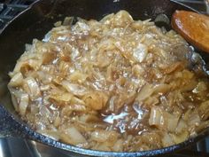 onions are being cooked in a skillet on the stove top with a wooden spoon