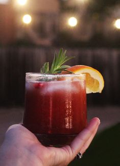 a hand holding a drink with an orange slice on the rim and garnish