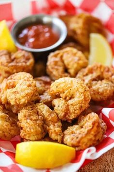 some fried food is on a red and white checkered plate with lemon wedges and ketchup