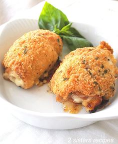 two crab cakes on a white plate with a green leaf