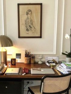 a desk with a chair, lamp and pictures on the wall above it in a home office