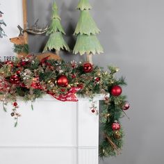 a mantel decorated for christmas with red and green ornaments on it, including pine trees