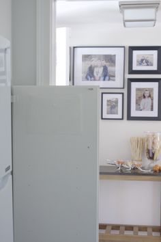 a white refrigerator freezer sitting next to a table with pictures on the wall behind it