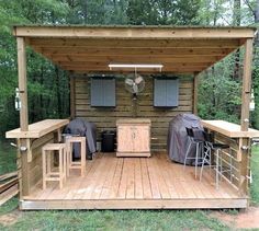 an outdoor kitchen on a wooden deck in the middle of a wooded area with grills and bar stools