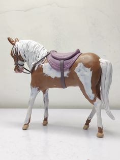 a brown and white toy horse with saddle on it's back, standing in front of a wall