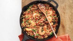 a skillet filled with shrimp and rice on top of a wooden cutting board next to a red napkin