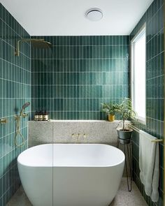 a bath tub sitting next to a window in a green tiled bathroom with gold trim