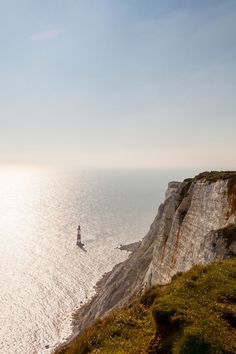 a lighthouse on the edge of a cliff overlooking the ocean with grass and cliffs below