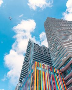 an airplane is flying in the sky over some tall buildings with multicolored windows