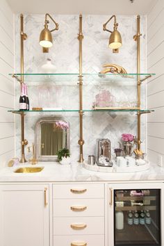 a white and gold bathroom with glass shelves, marble counter tops and brass fixtures on the wall