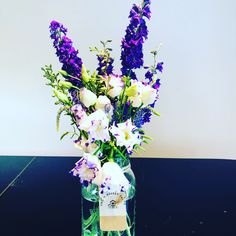 a vase filled with purple and white flowers on top of a black table next to a wall