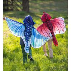 two children are walking in the grass with kites on their back and one is wearing a butterfly costume