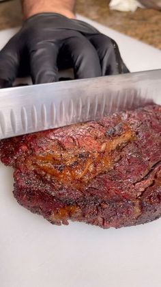 a person in black gloves is cutting meat with a large knife on a white board