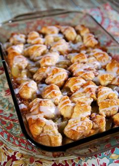 a casserole dish with cinnamon rolls covered in icing on a colorful tablecloth