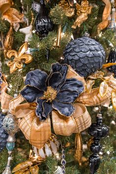 a christmas tree decorated with black and gold ornaments, pine cones, and bows is seen in this image