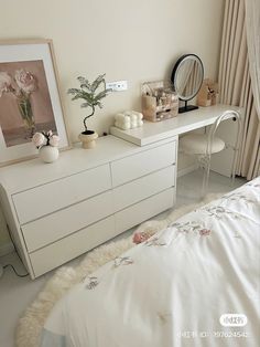 a white dresser sitting next to a bed with flowers on it and a mirror above it