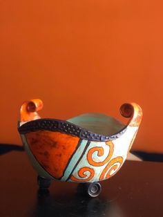 an orange and blue bowl sitting on top of a table next to a brown wall