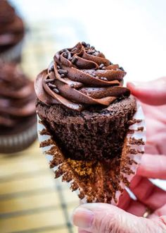 a person holding up a chocolate cupcake with frosting on the outside and inside