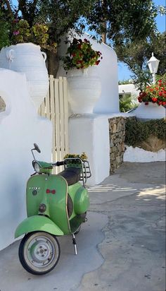 a green scooter parked in front of a white wall and potted plants