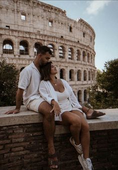 a man and woman are sitting on a wall in front of the colossion