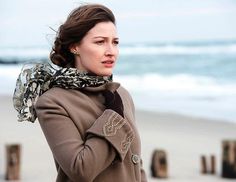 a woman standing on the beach wearing a scarf