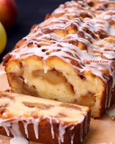 a close up of a sliced cake on a cutting board with apples in the background