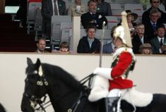 a man riding on the back of a black horse in front of a group of people