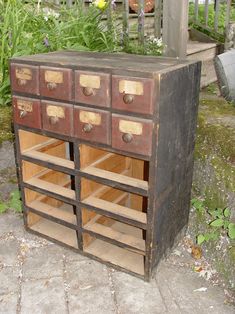 an old wooden cabinet with many drawers on it's sides and some flowers in the background