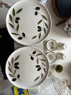 two plates with olives painted on them sitting on a table next to other dishes