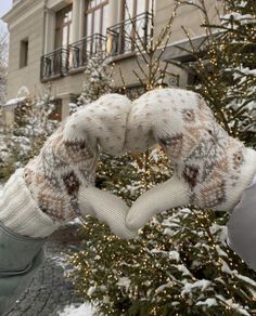 a person holding up a knitted heart shaped object in front of a christmas tree