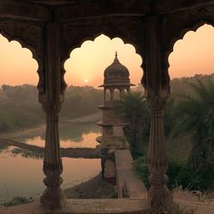 the sun is setting behind an ornate gazebo with water and trees in the background