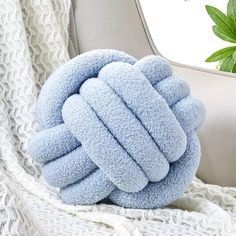 a blue knot pillow sitting on top of a white blanket next to a potted plant