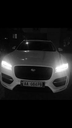 the front end of a white car with its headlights on at night in black and white