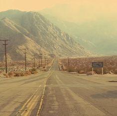 an empty road in the desert with mountains and telephone poles on either side that lead into the distance