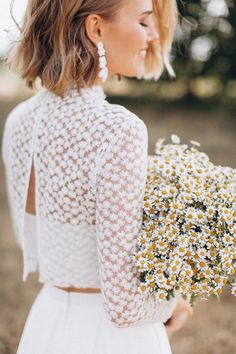 a woman in a white dress holding a bouquet of daisies