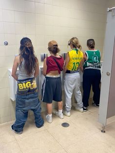 several people standing in line at a public bathroom stall with their backs to the wall