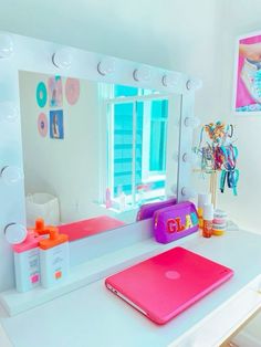 a white desk with a pink laptop on it and a large mirror in the background