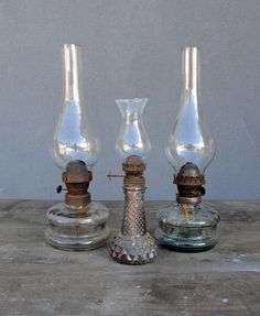 three glass vases sitting next to each other on top of a wooden table in front of a gray wall