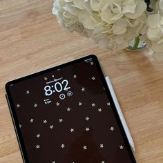 a tablet computer sitting on top of a wooden table next to a vase with white flowers