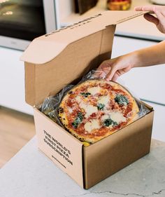 a person opening a pizza box on top of a counter