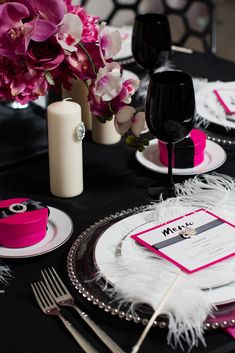 the table is set with black and white plates, silverware, and pink napkins