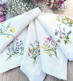 four napkins with flowers on them sitting next to a vase filled with wildflowers