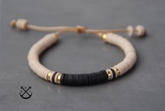 a white and black beaded bracelet on a gray surface with gold accents, sitting next to a string